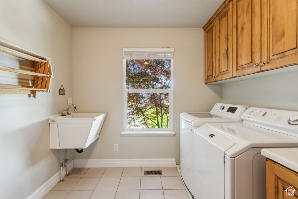 Laundry area with cabinet space, separate washer and dryer, light tile patterned floors, and baseboards