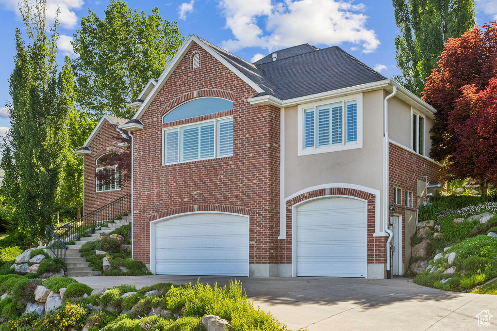 View of front facade featuring a garage, concrete driveway, brick siding, and stairs