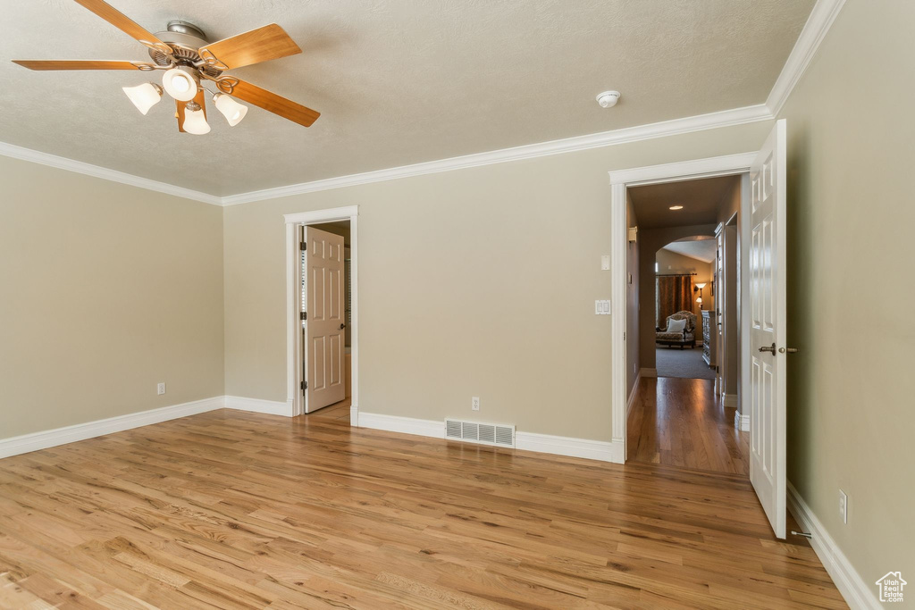 Unfurnished room featuring light wood-style floors, ornamental molding, a ceiling fan, arched walkways, and baseboards