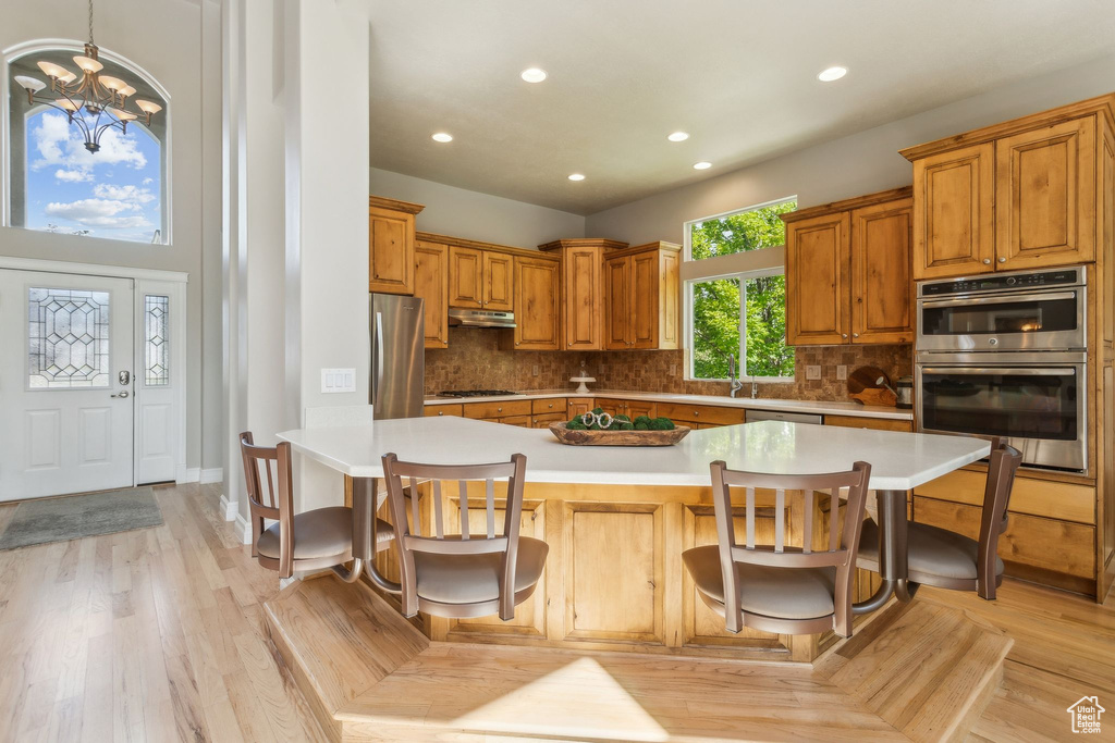 Kitchen with appliances with stainless steel finishes, under cabinet range hood, recessed lighting, light countertops, and a kitchen bar