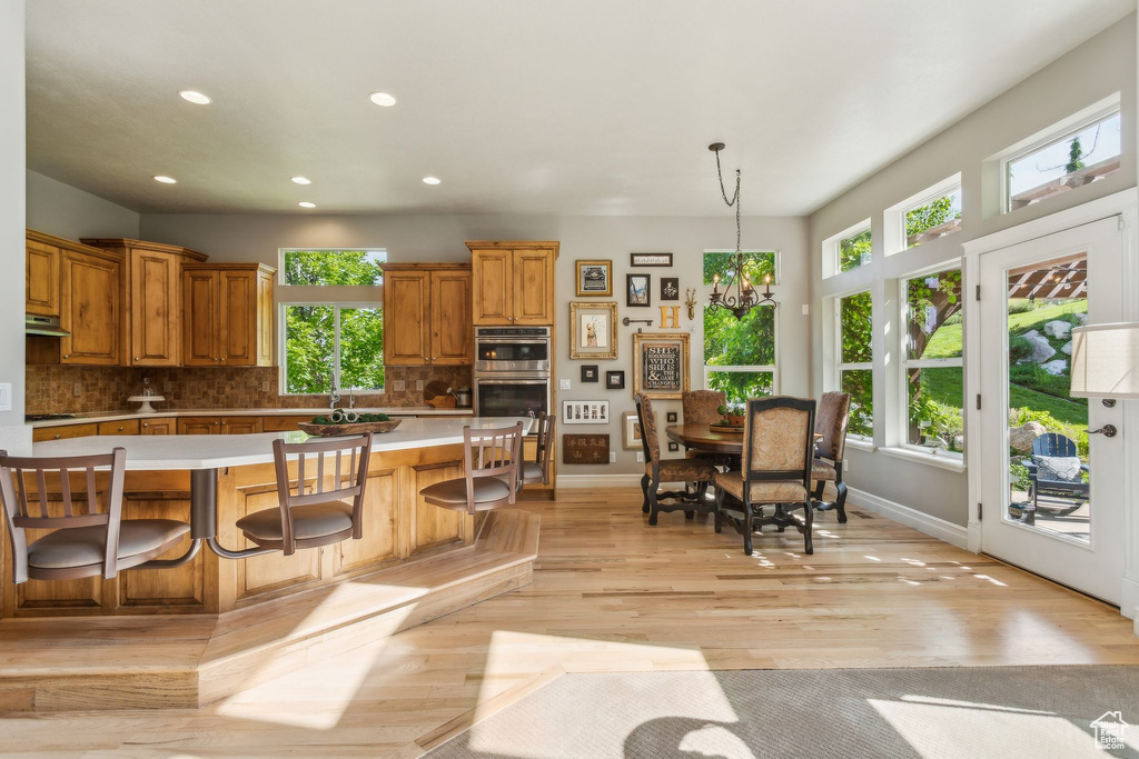 Kitchen featuring light countertops, double oven, decorative backsplash, under cabinet range hood, and recessed lighting