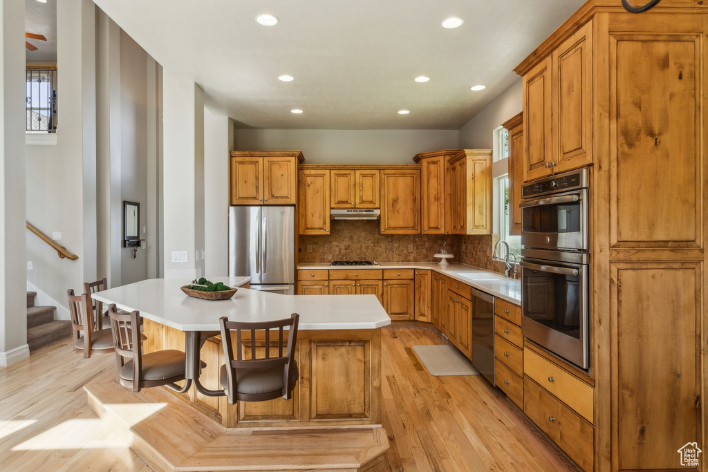 Kitchen with appliances with stainless steel finishes, recessed lighting, light wood-type flooring, decorative backsplash, and brown cabinets