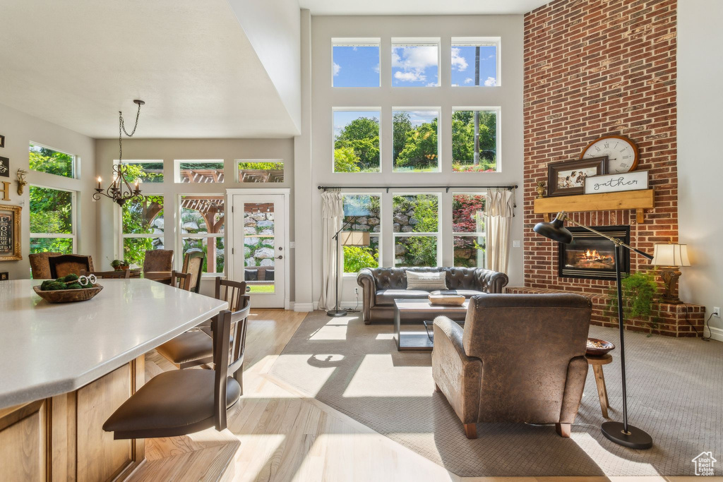 Living area with a high ceiling, a brick fireplace, a chandelier, plenty of natural light, and wood finished floors