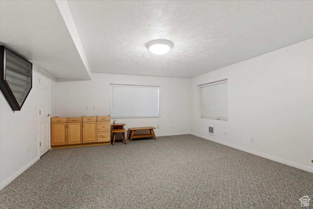 Bonus room with a textured ceiling, light carpet, and baseboards