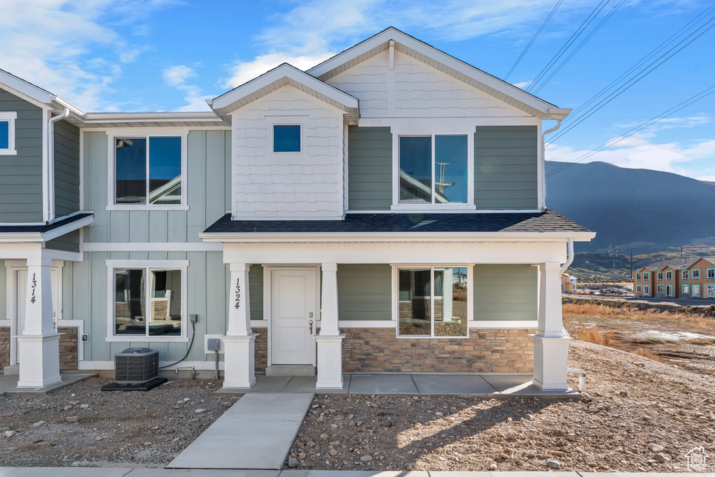 View of front of house featuring board and batten siding, cooling unit, a porch, a mountain view, and stone siding
