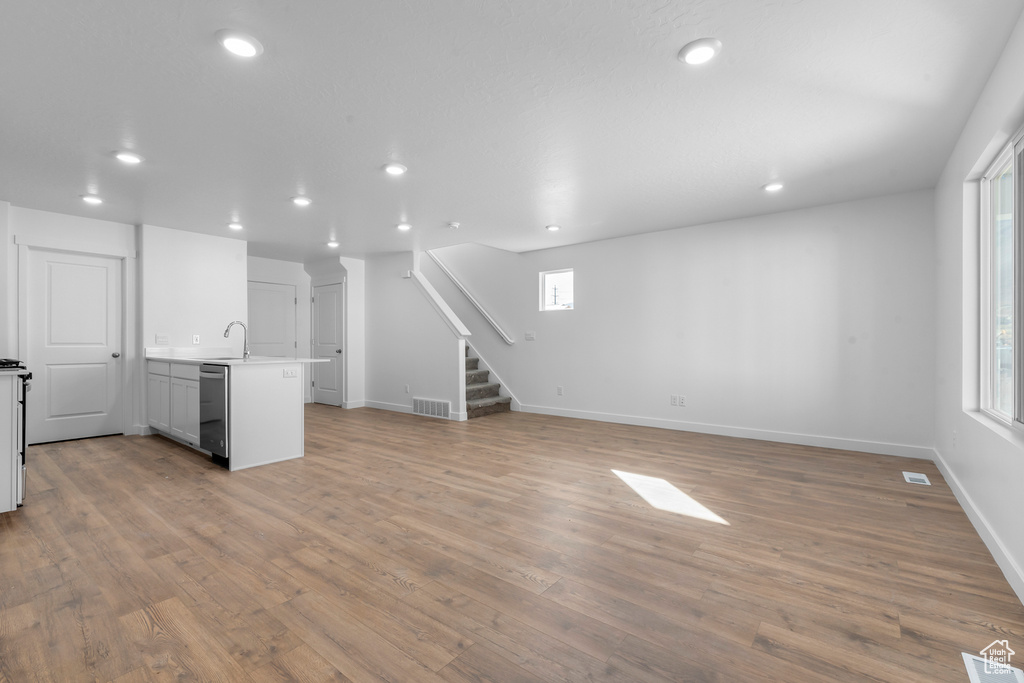 Unfurnished living room featuring stairway, recessed lighting, light wood-style floors, baseboards, and a sink