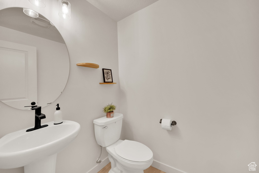 Half bathroom featuring a sink, toilet, baseboards, and wood finished floors