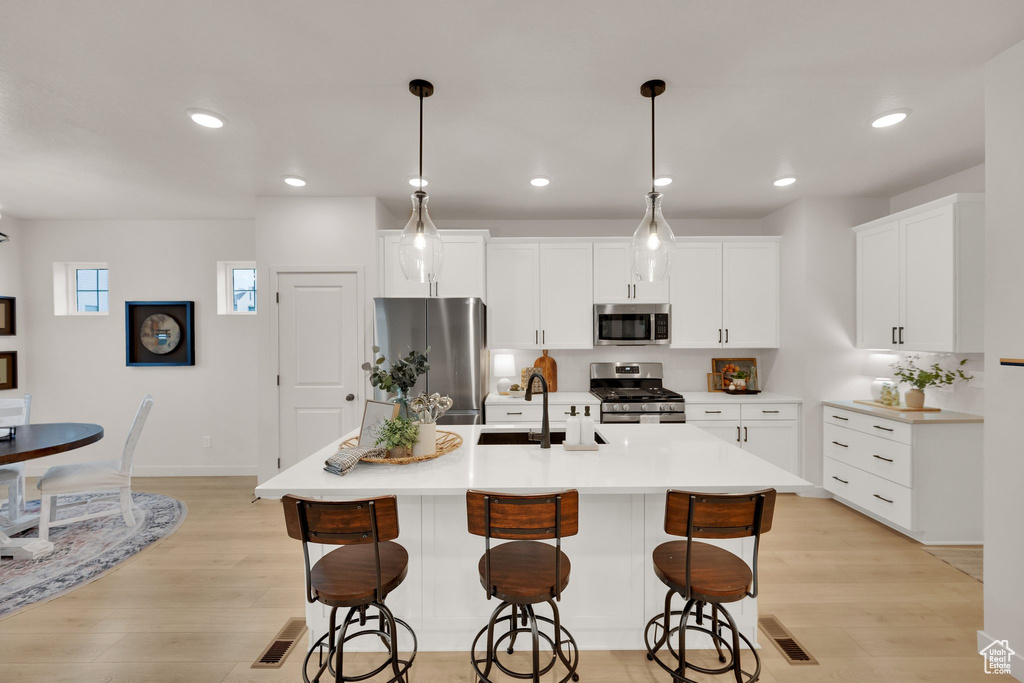 Kitchen featuring stainless steel appliances, a sink, light wood-style floors, a kitchen bar, and recessed lighting