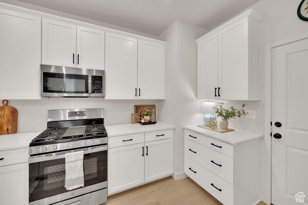 Kitchen featuring stainless steel appliances, light countertops, white cabinets, decorative backsplash, and light wood-style floors