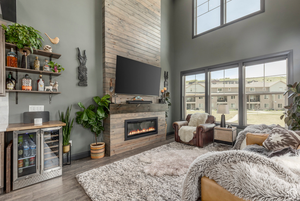 Living room with beverage cooler, a towering ceiling, wood finished floors, a glass covered fireplace, and bar area