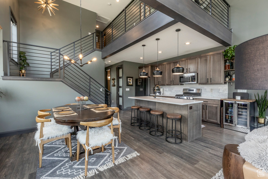 Dining room featuring beverage cooler, stairs, a towering ceiling, dark wood-style floors, and baseboards