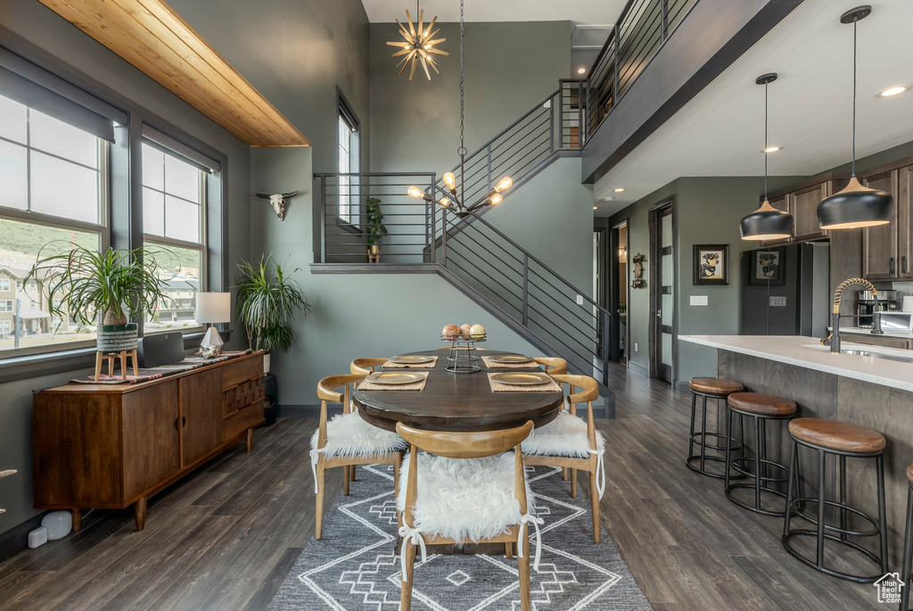 Dining area with stairs, a towering ceiling, dark wood-style floors, and baseboards