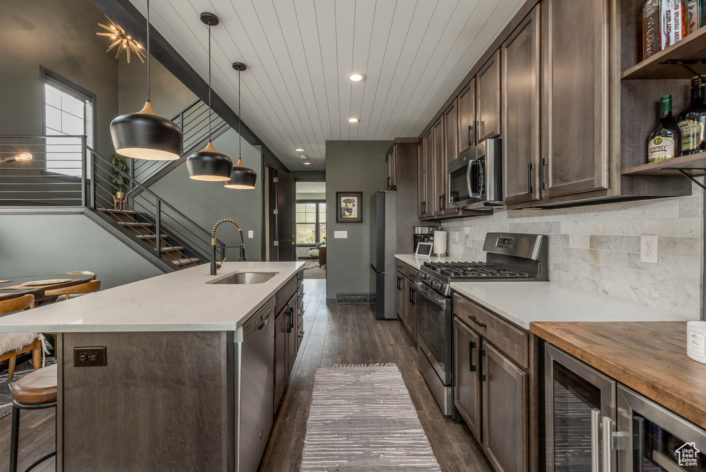 Kitchen featuring stainless steel appliances, a sink, open shelves, dark brown cabinets, and an island with sink