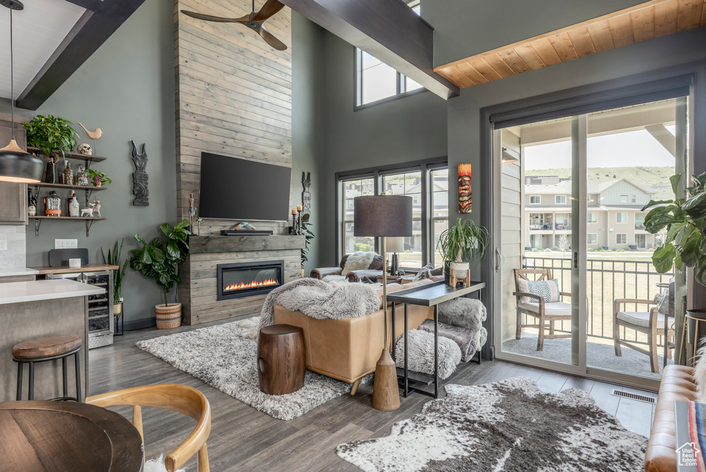Living room with a stone fireplace, wood finished floors, beam ceiling, and high vaulted ceiling