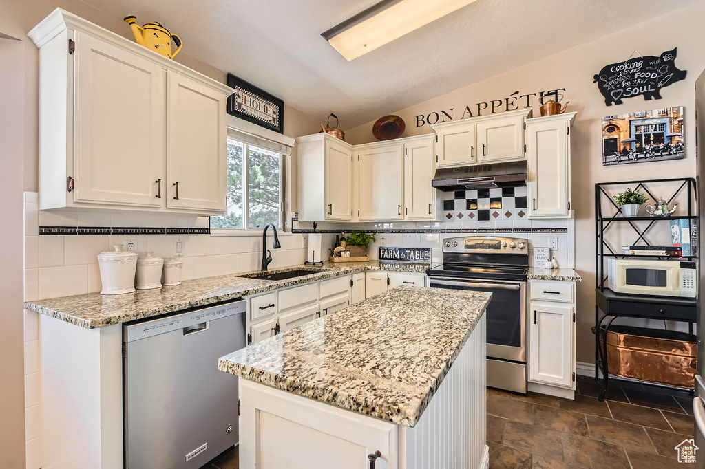 Kitchen featuring stainless steel appliances, a sink, under cabinet range hood, decorative backsplash, and lofted ceiling