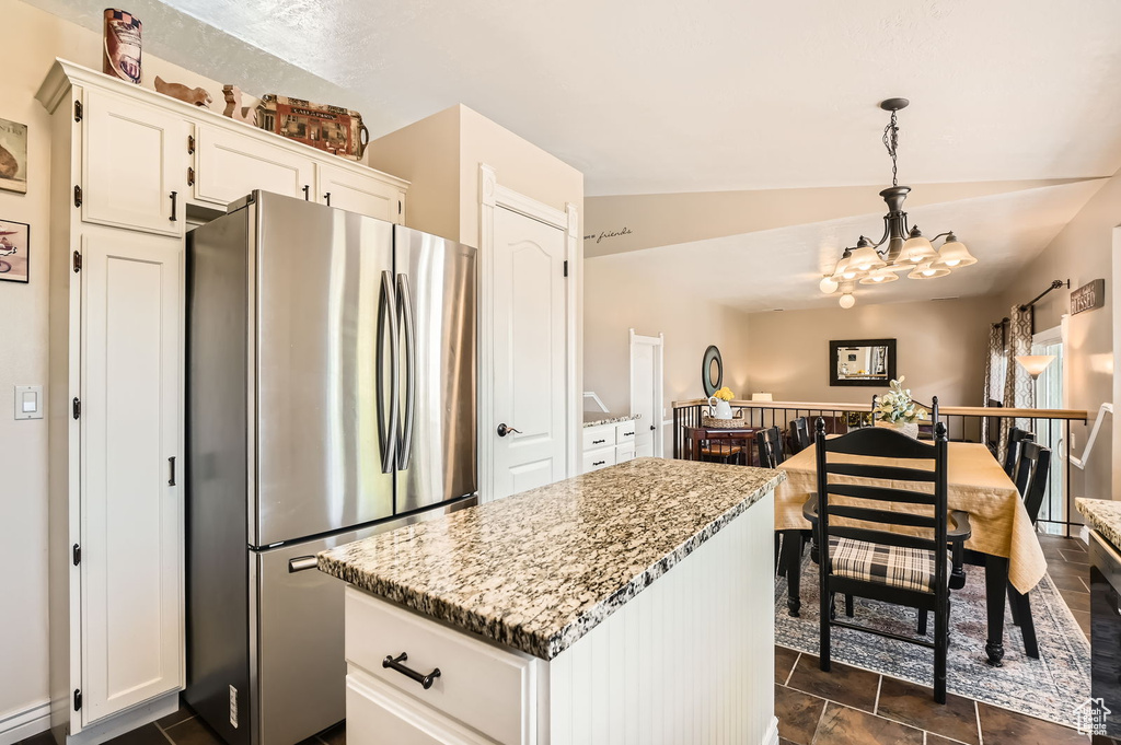 Kitchen with freestanding refrigerator, a chandelier, white cabinets, a center island, and light stone countertops