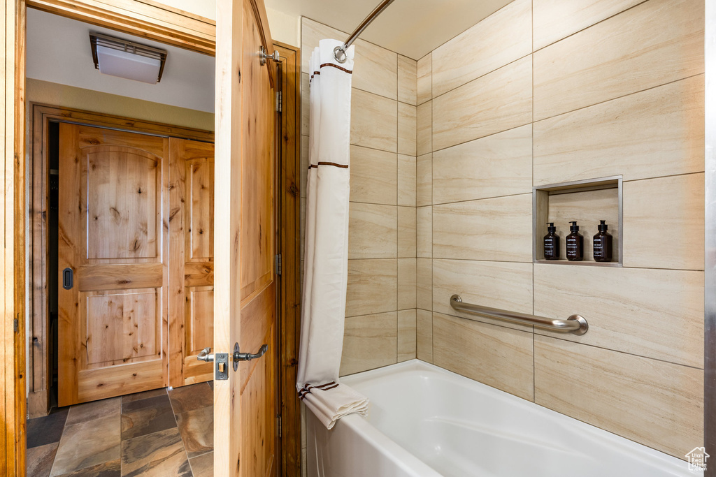 Full bath with shower / bathtub combination with curtain and stone finish flooring