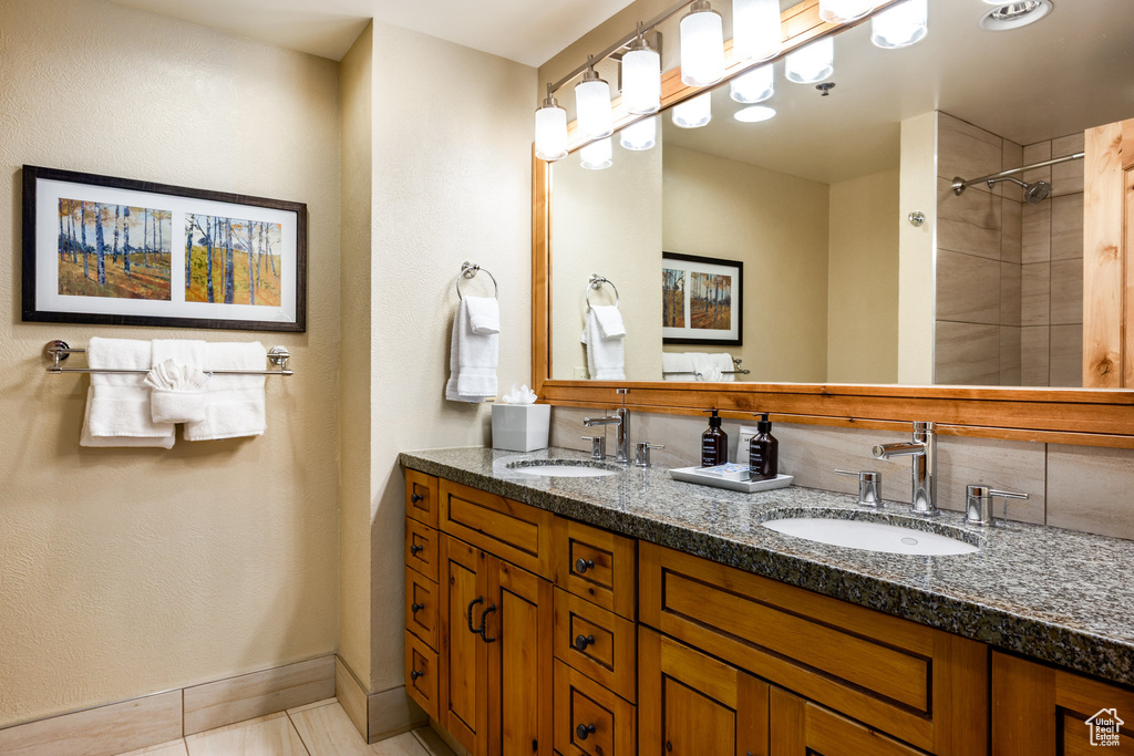 Full bathroom with double vanity, tile patterned flooring, tiled shower, and baseboards