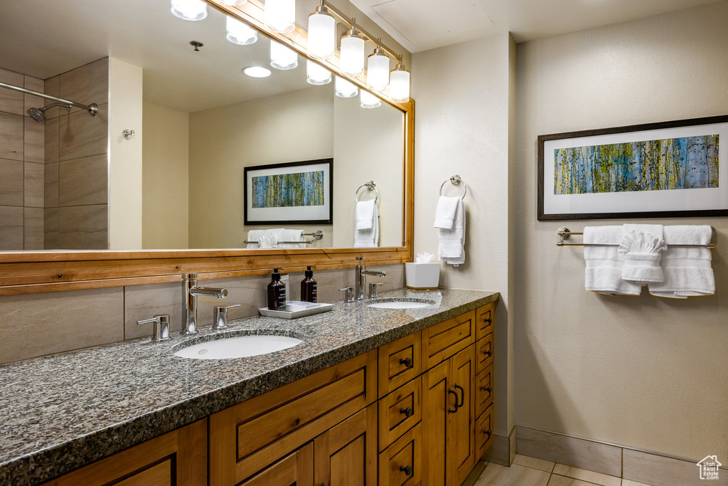 Full bath with double vanity, tile patterned floors, baseboards, and a shower