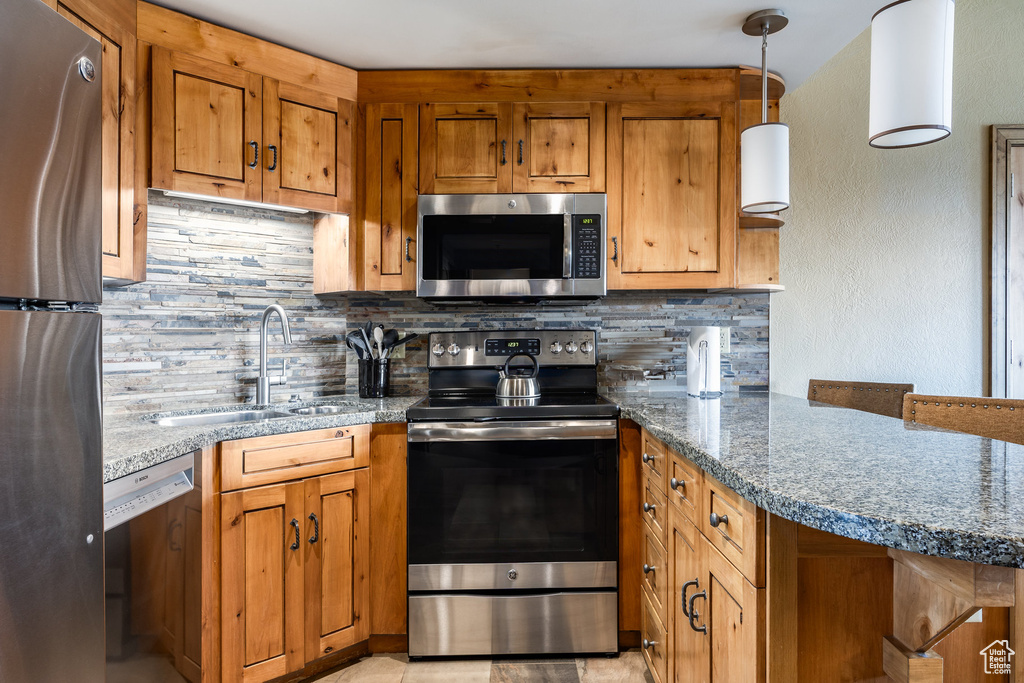Kitchen with appliances with stainless steel finishes, a sink, tasteful backsplash, and brown cabinetry