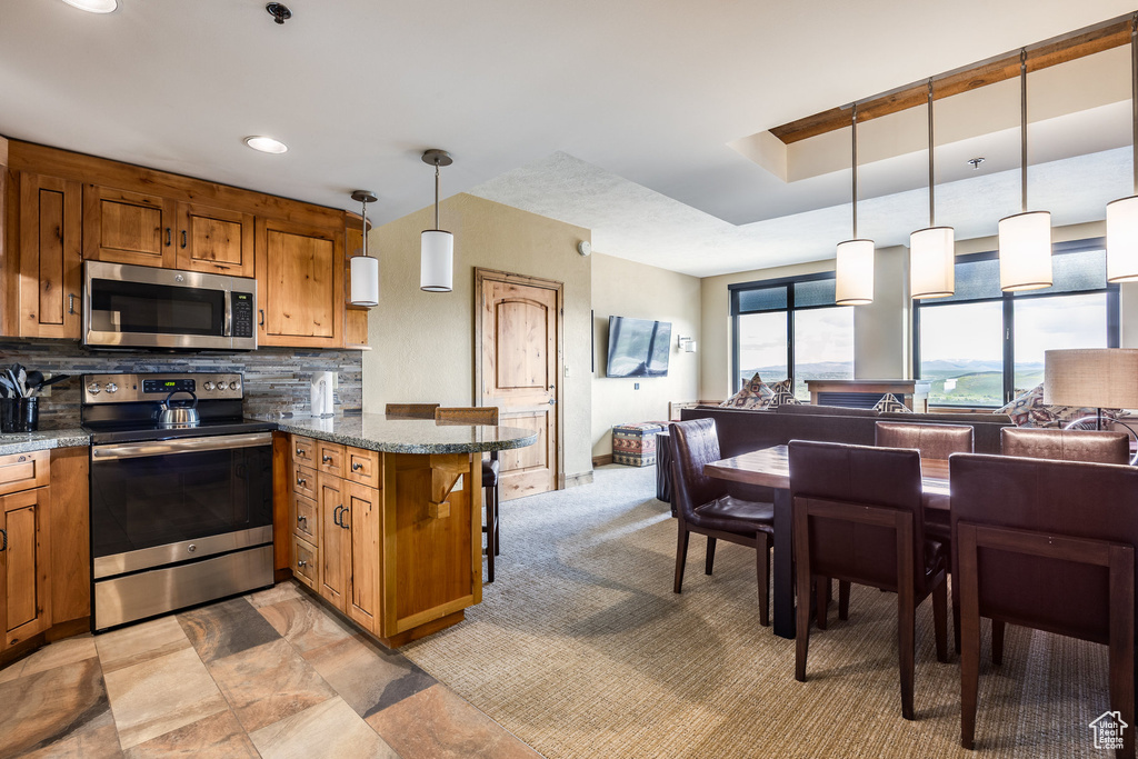 Kitchen featuring stainless steel appliances, brown cabinetry, open floor plan, a peninsula, and backsplash