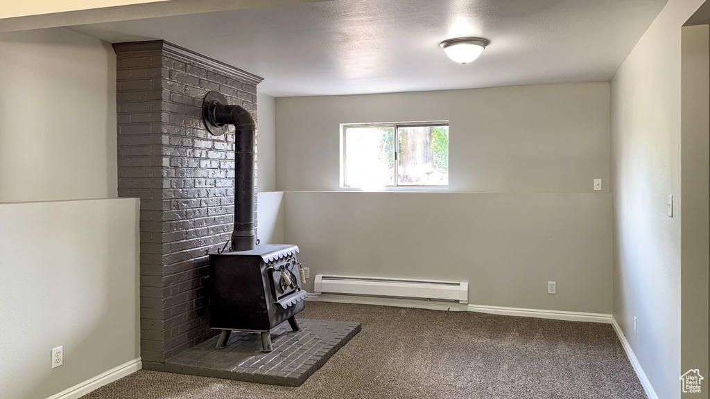 Unfurnished room featuring baseboard heating, a wood stove, carpet flooring, and baseboards