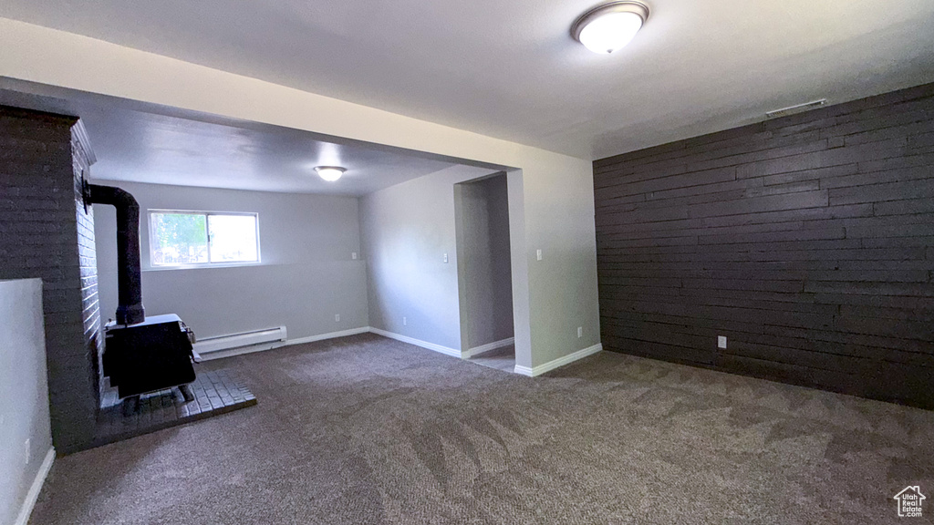 Below grade area featuring a wood stove, baseboard heating, carpet floors, baseboards, and an accent wall