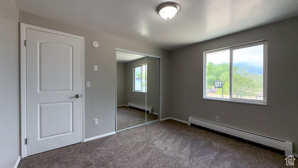 Unfurnished bedroom featuring baseboard heating, carpet, a closet, baseboards, and a textured ceiling