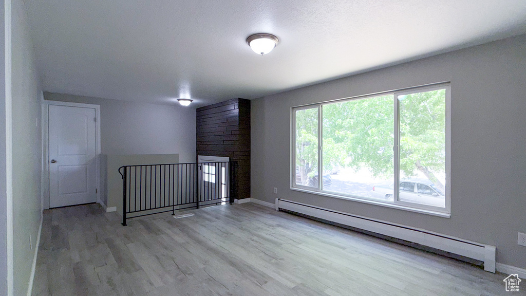 Unfurnished room featuring baseboard heating, wood finished floors, and baseboards