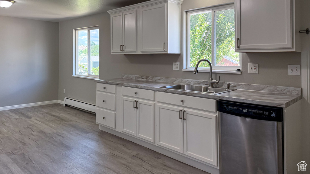 Kitchen featuring stainless steel dishwasher, a sink, a baseboard radiator, light wood-type flooring, and light countertops
