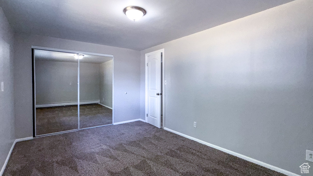 Unfurnished bedroom with a baseboard radiator, carpet, baseboards, and a closet