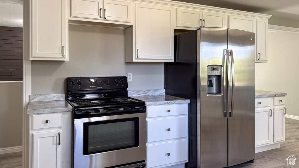 Kitchen with appliances with stainless steel finishes, light countertops, light wood-type flooring, and white cabinetry