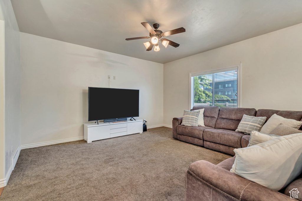 Carpeted living room with a ceiling fan and baseboards