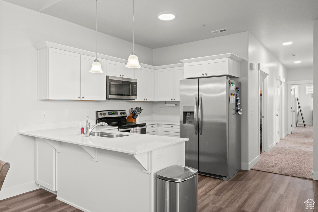 Kitchen featuring appliances with stainless steel finishes, a peninsula, dark wood-type flooring, a sink, and baseboards