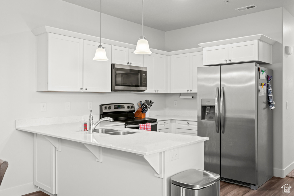 Kitchen featuring appliances with stainless steel finishes, a peninsula, dark wood-type flooring, a sink, and a kitchen breakfast bar