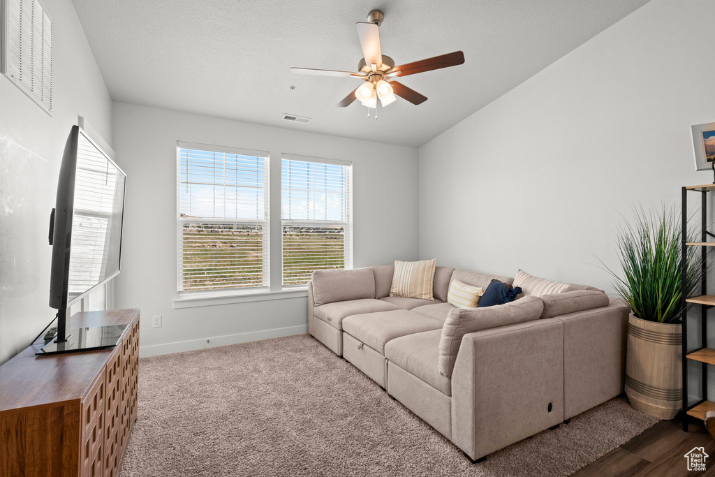Carpeted living area with ceiling fan, baseboards, and vaulted ceiling