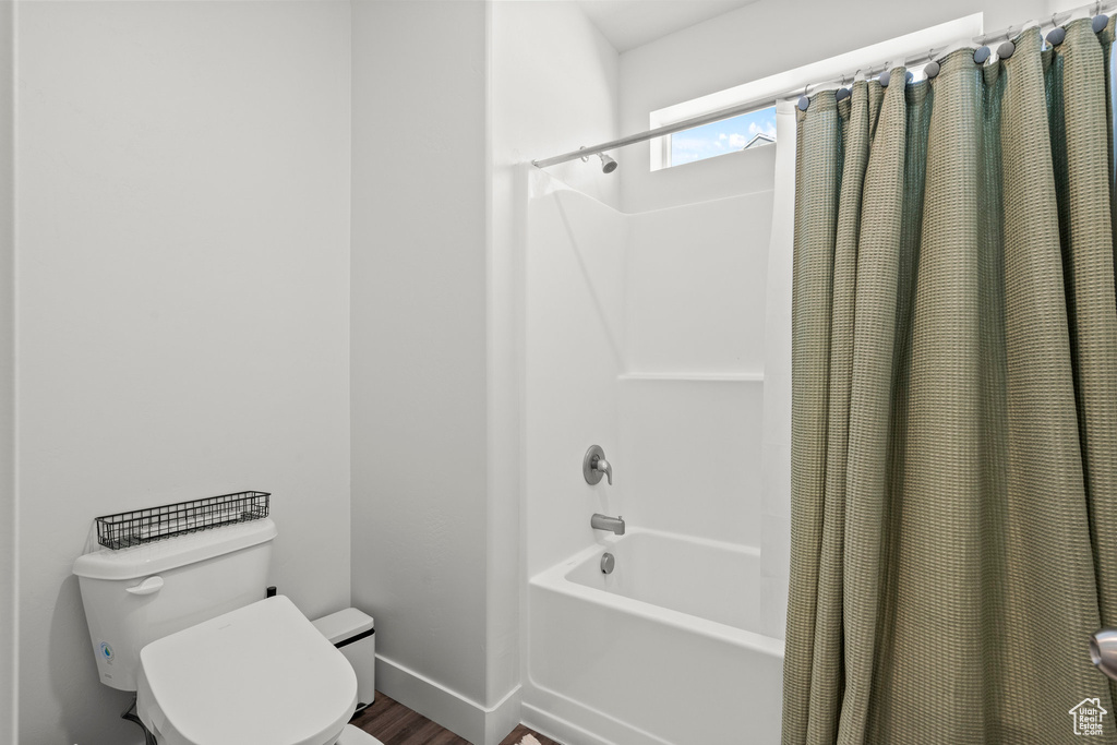 Bathroom featuring shower / tub combo with curtain, toilet, wood finished floors, and baseboards