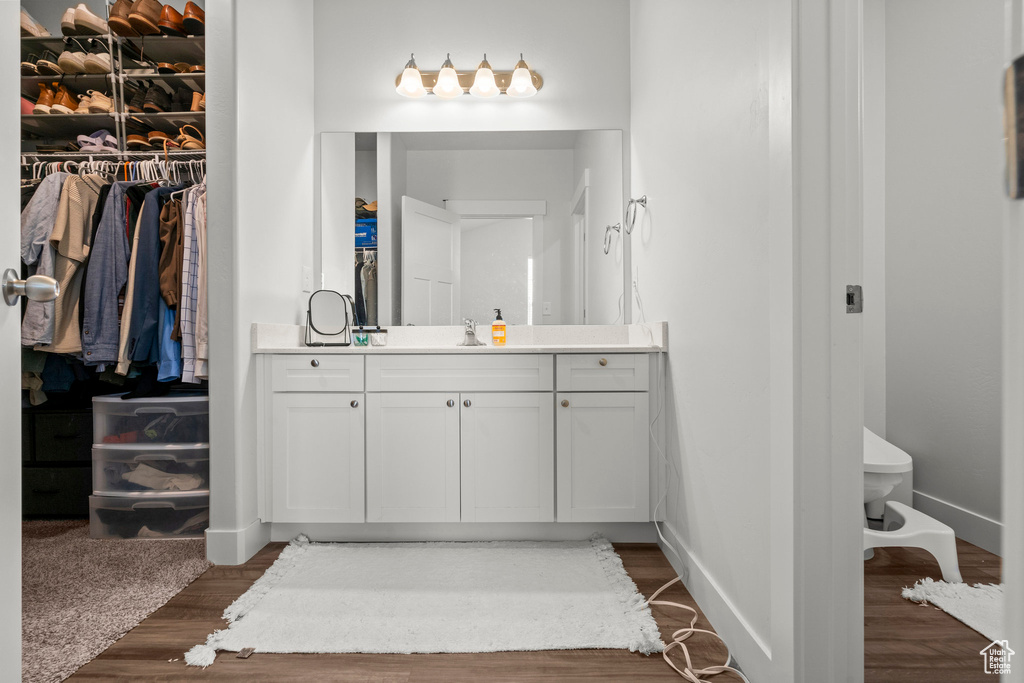 Bathroom featuring vanity, toilet, wood finished floors, baseboards, and a spacious closet