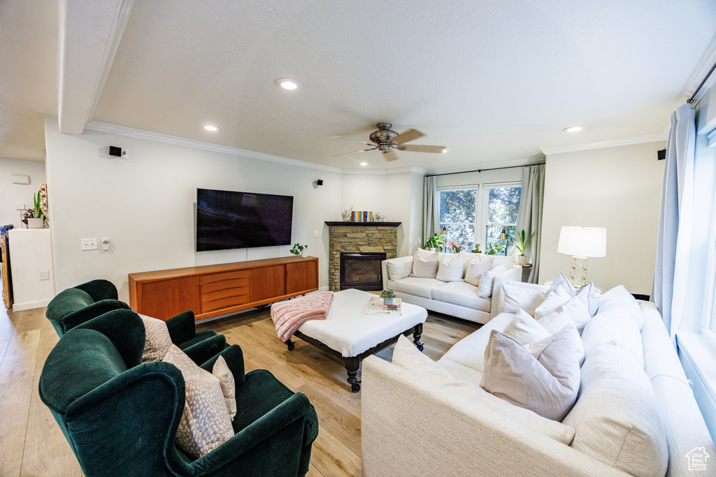 Living room with a ceiling fan, recessed lighting, light wood finished floors, a stone fireplace, and ornamental molding