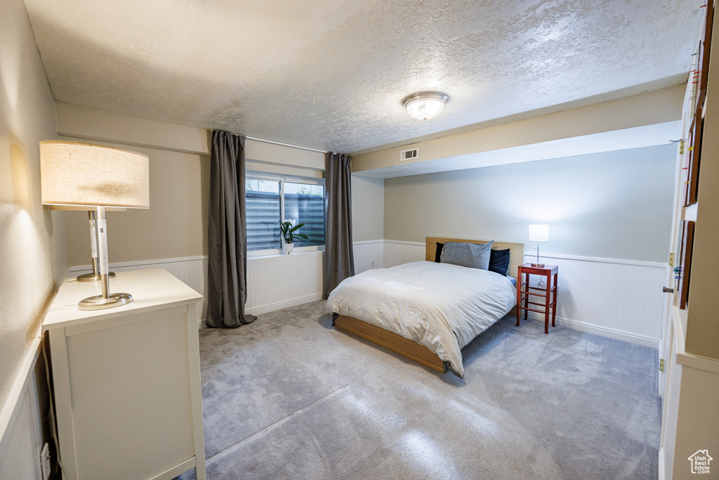 Bedroom featuring wainscoting, a textured ceiling, and light colored carpet