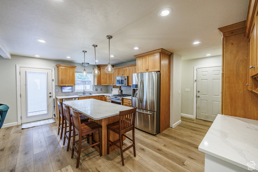 Kitchen featuring appliances with stainless steel finishes, a sink, light wood finished floors, baseboards, and a kitchen breakfast bar