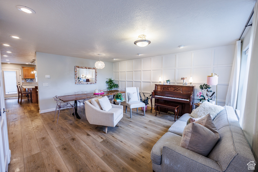 Living room featuring a decorative wall, light wood-type flooring, recessed lighting, a textured ceiling, and a chandelier