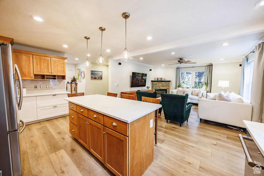 Kitchen featuring freestanding refrigerator, a ceiling fan, light wood-style floors, a center island, and a fireplace