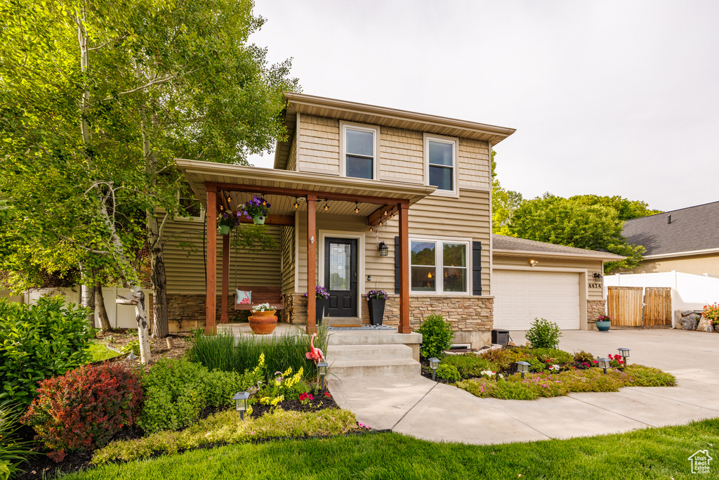 View of front of property with driveway, stone siding, a garage, and covered porch