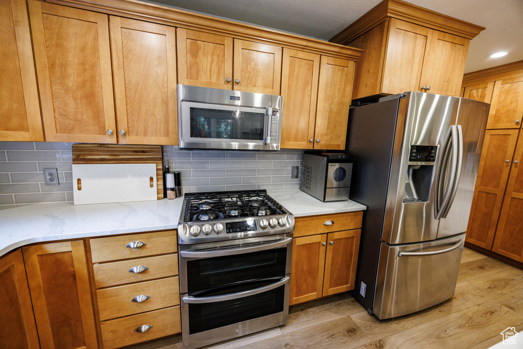 Kitchen with appliances with stainless steel finishes, brown cabinets, light stone counters, and recessed lighting