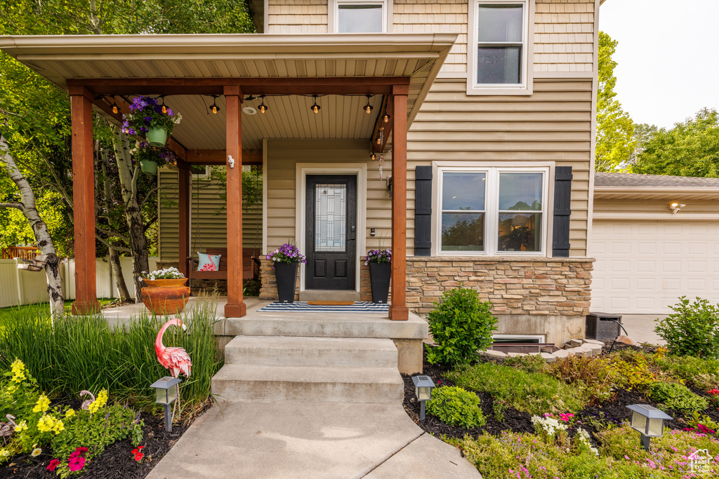 View of exterior entry featuring stone siding, an attached garage, and covered porch
