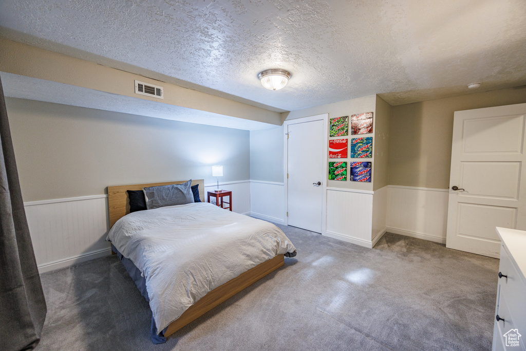 Carpeted bedroom with a wainscoted wall, a textured ceiling, and a closet