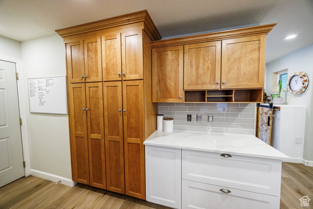 Kitchen with light wood-style flooring, backsplash, open shelves, light stone countertops, and baseboards