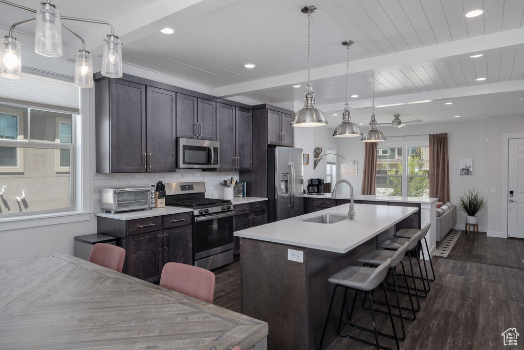 Kitchen featuring stainless steel appliances, dark wood-type flooring, a sink, a kitchen island with sink, and a breakfast bar area