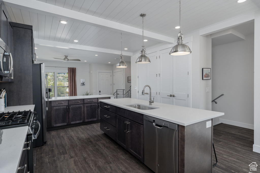 Kitchen with appliances with stainless steel finishes, a sink, dark wood finished floors, a kitchen island with sink, and light countertops